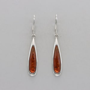 May include: A pair of silver teardrop earrings with amber stones.