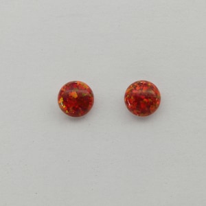 May include: A pair of small, round, red earrings with a sparkly, iridescent finish.