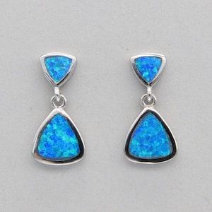 May include: A pair of silver dangle earrings with blue opal triangle stones. The earrings have a smaller triangle stone at the top and a larger triangle stone at the bottom.