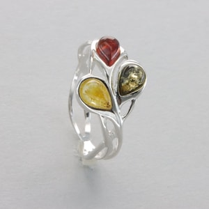 May include: A silver ring with a delicate, leafy design features three teardrop-shaped amber stones in shades of red, yellow, and green.