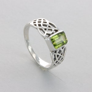 May include: A silver ring with a green gemstone set in a Celtic knot design.