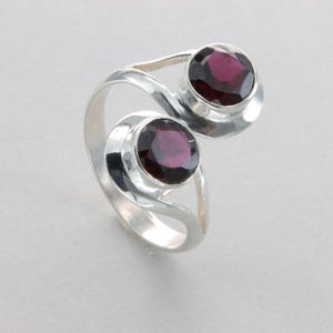 May include: A silver ring with two round, dark purple gemstones set in a swirling design.