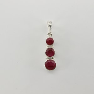 May include: A silver pendant with three round red ruby gemstones hanging in a vertical line.