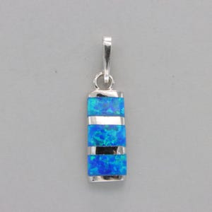 Peut inclure: Un pendentif en argent avec une pierre d'opale bleue. L'opale est coupée en trois sections rectangulaires avec des bandes d'argent entre chaque section.