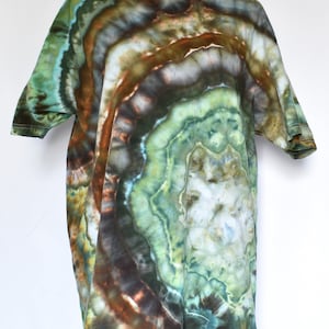 May include: A short-sleeved t-shirt with a unique tie-dye pattern. The shirt features a blend of green, brown, and blue hues, creating a marbled effect. The fabric appears soft and comfortable, with a classic crew neck and short sleeves.