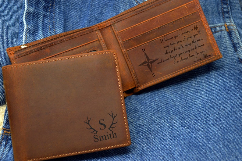 May include: A brown leather wallet with a compass and the text "Wherever your journey in life may take you, I pray you'll always be safe, enjoy the ride, and never forget your way back home. I'm always here for you... Love, Mom" engraved on the inside. The outside of the wallet has a personalized inscription with the letter "S" and the name "Smith" with antlers on either side.
