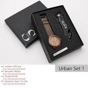 May include: A black gift box set containing a wooden watch with a brown leather strap, a black pocket knife, and a silver tie clip. The watch face has a wood grain design. The box is labeled "Silva" and "Urban Set 1".