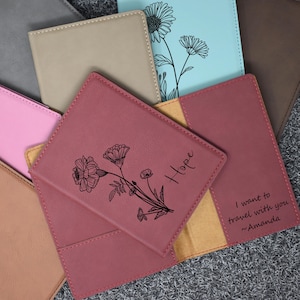 May include: A burgundy leather passport holder with a floral design and the word "Hope" engraved on the front. The inside of the holder has a tan leather pocket with the text "I want to travel with you ~Amanda".