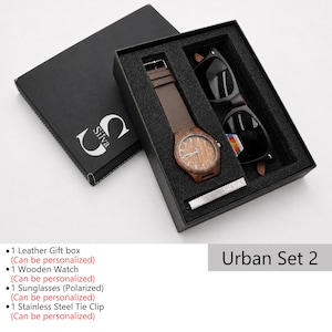 May include: An open black gift box set containing a wooden watch with a brown leather band, black sunglasses, and a silver tie clip. The watch face has a wood grain design. The box is labeled "Silva" and "Urban Set 2".