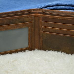 May include: A brown leather wallet with a clear plastic window for an ID card. The wallet has multiple card slots and a fold-over closure.