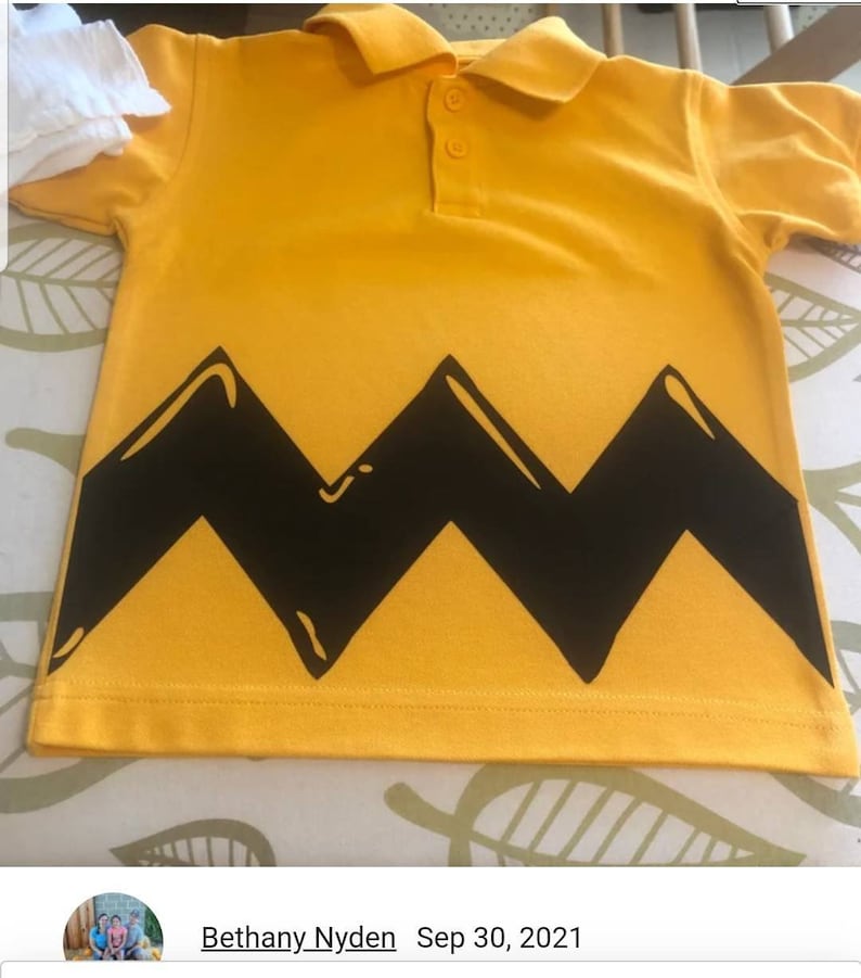 K&ouml;nnte beinhalten: Gelbes Poloshirt mit einem schwarzen Zickzackmuster am unteren Rand. Das Shirt hat einen Kragen und Kn&ouml;pfe.