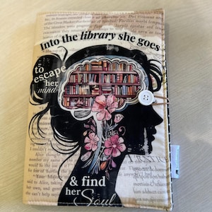 Puede incluir: Una ilustración en blanco y negro de la silueta de una mujer con una estantería dentro de su cabeza. El texto "Into the library she goes to escape her mind & find her soul" está impreso en la imagen. La imagen está impresa en una cubierta de diario de tela.