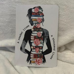 May include: A silhouette of a person with a stack of books and pink roses forming their body. The text "A reader lives a thousand lives" is on the left and right sides of the image.