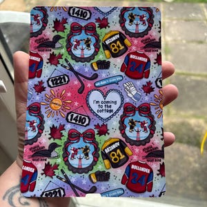 Peut inclure: Un objet décoratif rectangulaire avec un motif coloré présentant des graphiques sur le thème du hockey, notamment des maillots, des crosses et le texte "I'm coming to the cottage". Le motif comprend des feuilles d'érable, des nœuds et les chiffres 1410, 1221, 81 et 24.