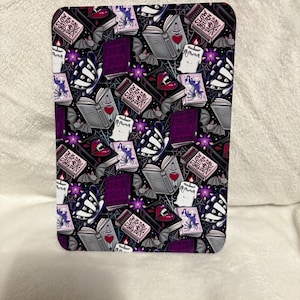 May include: A rectangular item with a repeating pattern of gothic imagery. The design includes books, candles, bats, and the text "SLOW BURN". The colour scheme is predominantly black, purple, and white. The overall aesthetic suggests a theme related to witchcraft or the occult.