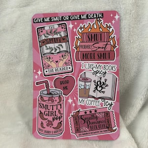 Op de afbeelding: Een roze achtergrond met een verzameling stickers met verschillende ontwerpen. De stickers bevatten een boek met de tekst "SMUT" erop, een blikje met de tekst "SMUTTY GIRL pop" erop, een koffiebeker met de tekst "MY COFFEE Icy" erop en een kaartje met de tekst "Smutty Romance Book Club" erop.