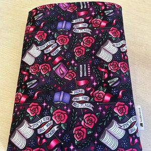 Może przedstawiać: Czarna, materiałowa osłonka na książkę z powtarzającym się wzorem czerwonych róż, otwartych książek i gwiazd. Tekst "Here for the Red Flags" powtarza się w całym wzorze.