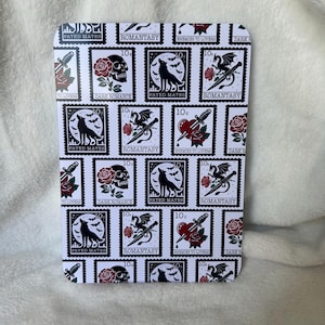 May include: A white background with a repeating pattern of black and white postage stamps. Each stamp features a different dark romance themed image, including a skull, a wolf, a dragon, a dagger, and a heart. The text "ROMANTASY" and "FATED MATES" appears on the stamps.