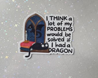 Op de afbeelding: Een sticker met de tekst "I THINK a lot of my PROBLEMS would be solved if I had a DRAGON." De sticker toont een zwarte kat, een draak, een kaars en boeken. De achtergrond is een sterrennacht.