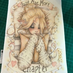 Op de afbeelding: Een witte boekhoes met een fantasievolle illustratie van een meisje dat een boek leest. Het meisje heeft blond haar en draagt een witte trui. De tekst "Just One More Chapter" staat op de hoes gedrukt.