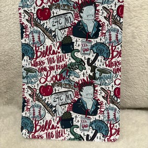 Puede incluir: Un cuaderno rectangular con un fondo blanco y un patrón repetido de ilustraciones y texto. El diseño incluye imágenes de un vampiro, manzanas, pelotas de béisbol y texto que dice "Bella? Where the hell have you been?" y "Forks, Washington".