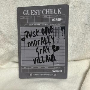 May include: A black and white guest check with the text "Just one morally gray villain" written in black marker.