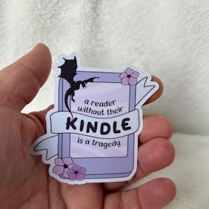 Op de afbeelding: Een paarse en witte sticker met een zwart silhouet van een draak en de tekst "a reader without their KINDLE is a tragedy".