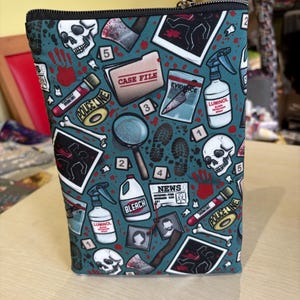 May include: A teal zipped cosmetic bag featuring a crime scene investigation theme. The pattern includes skulls, blood splatters, evidence markers, and the words "CASE FILE", "EVIDENCE", "BLEACH", and "LUMINOL".