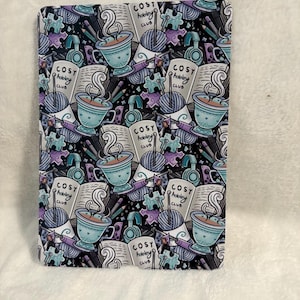 Könnte beinhalten: Ein rechteckiger Gegenstand mit einem sich wiederholenden Muster aus türkisfarbenen Tassen, Büchern, Garn, Kopfhörern und dem Text "COSY hobby CLUB". Der Hintergrund ist schwarz mit lila und türkisfarbenen Akzenten.