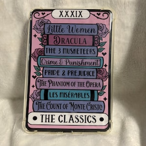 May include: Clear phone case with a pink and purple design featuring the text "XXXIX" and the words "Little Women", "Dracula", "The 3 Musketeers", "Crime & Punishment", "Pride & Prejudice", "The Phantom of the Opera", "Les Miserables", "The Count of Monte Cristo", and "The Classics".