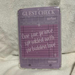 Op de afbeelding: Een paarse en witte telefoonhoes met een gastcheck-ontwerp. De tekst op de hoes luidt "GUEST CHECK" en "One fae prince, sprinkled with forbidden love".