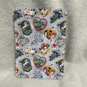 Op de afbeelding: Een rechthoekige onderzetter met een grijze achtergrond en een herhalend tattoo-achtig ontwerp. Het ontwerp bevat afbeeldingen van een gebakken ei, een ring, een hobbitgat, een eenhoorn, een roos en een vurige demon. De tekst bevat "BREAKFAST" en "YOU SHALL NOT PASS".