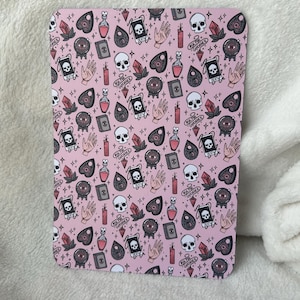 May include: Pink background with a repeating pattern of black and white illustrations of skulls, crystals, eyes, hearts, and bottles. The text "Ask the Guidance" is repeated throughout the pattern.