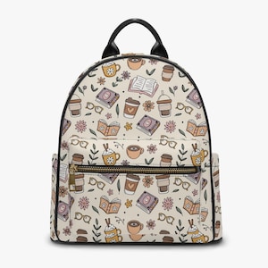 May include: Cream-colored backpack with a repeating pattern of books, coffee cups, eyeglasses, and flowers. The backpack has a black handle and trim, a front zipper pocket, and gold-colored zippers.