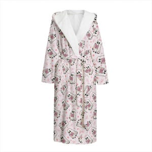 May include: A white hooded robe with a repeating pattern of cartoon ghosts wearing pink scarves and holding books. The robe has a white interior and a matching belt. The design includes pink stars and bows.