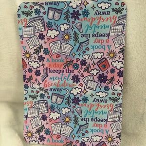 May include: A pink and blue patterned background with a repeating design of books, calendars, clouds, and stars. The text "A book a day keeps the mental breakdown away" is repeated throughout the design.