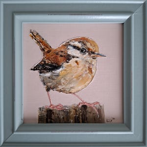Könnte beinhalten: Gerahmtes Gemälde eines kleinen Vogels mit braunen, beigen und weißen Federn, der auf einem Holzpfosten sitzt. Der Vogel ist mit sichtbaren Pinselstrichen vor einem blassrosa Hintergrund gemalt. Der Rahmen ist blau-grau.