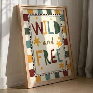 May include: A framed art print with the words "WILD and FREE" in colourful letters. The artwork features a cream-coloured background with a decorative border of squares in various colours. The frame is made of light-coloured wood.