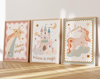 May include: Three framed art prints with a whimsical theme. One features a star with the text "Shine bright", another a castle with "believe in magic", and the last a unicorn with the name "Amelia". The prints have a soft color palette.