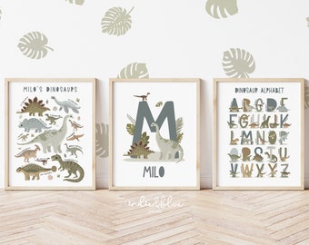 May include: Three framed prints with a dinosaur theme. The left print features a variety of dinosaurs with the text "Milo's Dinosaurs". The middle print features a large letter "M" with a dinosaur and the text "Milo". The right print features a dinosaur alphabet with the text "Dinosaur Alphabet".