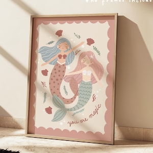 May include: A framed print depicting two cartoon mermaids with blue and pink hair, and mermaid tails in pink and green hues. The print has a scalloped border and the words "you are magic". The text "+ no frames included" is also visible.