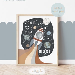 May include: A printable art print featuring a rocket ship flying through space with the text "Zoom to the moon". The rocket ship is white with red and brown accents. The background is black with stars, planets, and a moon.