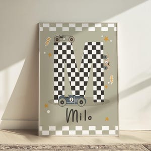 May include: A green and white chequered letter M with a blue racing car on the bottom and a grey racing car on top. The letter is surrounded by yellow stars and lightning bolts. The name Milo is written below the letter.