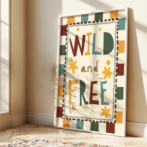 May include: A framed art print displaying the words "WILD and FREE" in a vibrant, whimsical font. The artwork has a cream backdrop, a decorative border, and a checkered pattern in brown, green, and orange hues.