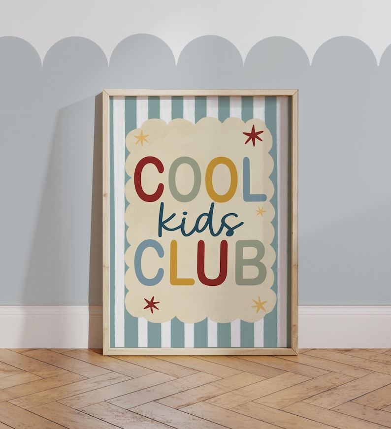 May include: A framed print with the words "COOL kids CLUB" in colorful letters. The background of the print is a cream color with a scalloped edge, set against a striped blue and white background. The frame is a light wood color.