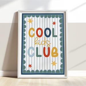 May include: A framed print with the words "COOL kids CLUB" in colorful letters. The background has vertical stripes, and the border is scalloped. Stars are scattered around the text.