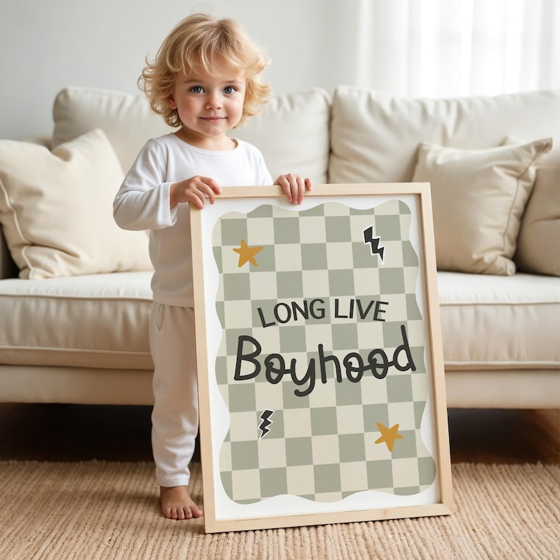 May include: A child is holding a framed print with a chequered background and the text "Long Live Boyhood". The print has a wavy border and features yellow stars and lightning bolts.