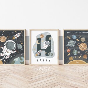 May include: Three space-themed prints with a dark blue background and gold stars. The first print features an astronaut floating in space with planets and a rocket. The second print features the letter H with an astronaut inside and the name Harry below. The third print features a solar system with planets and the text "Harry's Solar System".