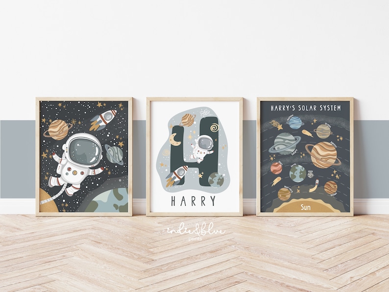 May include: Three space-themed prints with a dark blue background and gold stars. The first print features an astronaut floating in space with planets and a rocket. The second print features the letter H with an astronaut inside and the name Harry below. The third print features a solar system with planets and the text "Harry's Solar System".