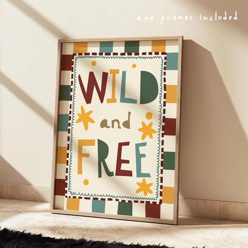 May include: A framed art print displaying the words "WILD and FREE" in a vibrant, whimsical font. The print has a cream background with a decorative border and star motifs. The frame is a light wood colour.